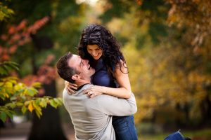 Engagement couple hugging in the woods, he lifts her