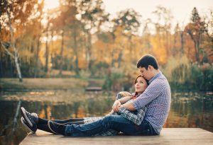 Engagement couple hugging by the lake sitting on a dock