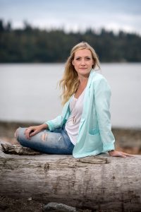 blonde girl sitting on a log at the beach